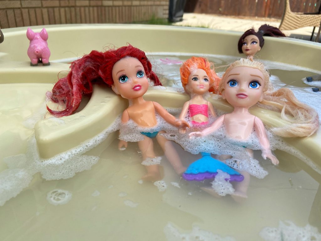 Three dolls sitting in water table. Bubbles added for easy warm weather activity