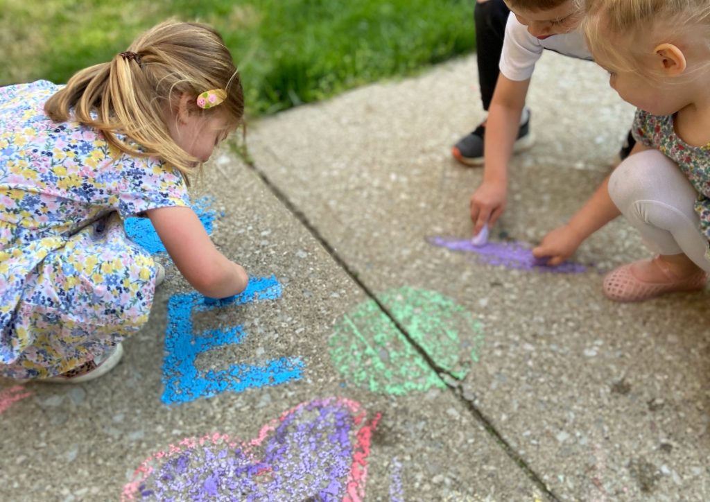 warm weather activities - 3 young children writing with chalk on sidewalk