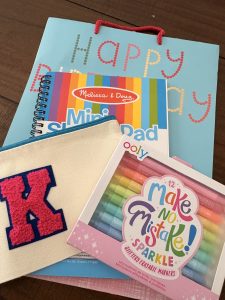 Photo of a blue Happy Birthday gift bag. On top is a mini notebook, a package of markers, and a canvas pouch with a K on it.