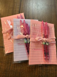 A picture of three notebooks - pink, purple, and pink. Each package includes a pink pen tied with a ribbon.
