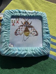 Cross Stitch hoop showing a half finished lightening bug with a green towel background